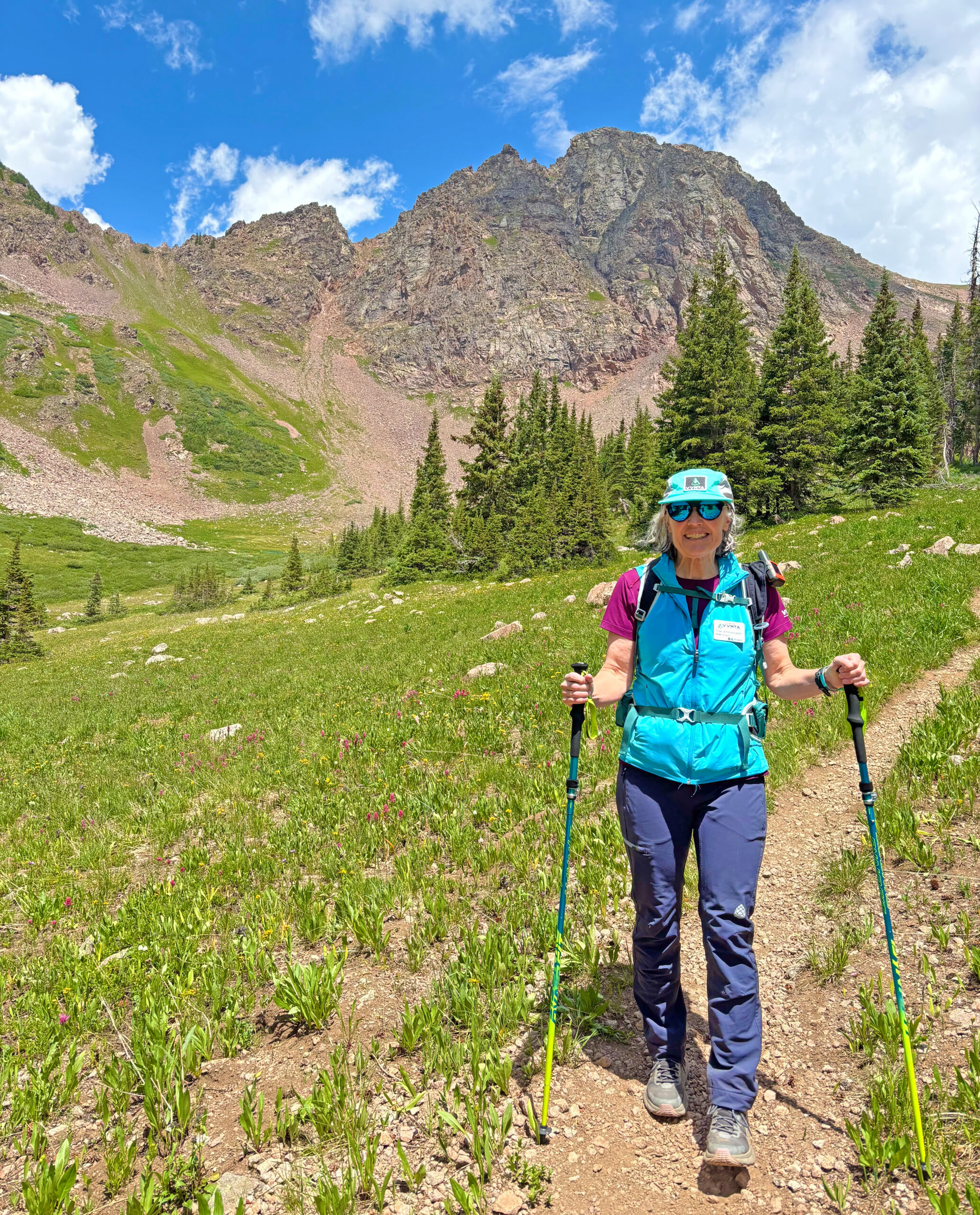 VVMTA Trail Ambassador hiking Eagle County backcountry trail with summer wildflowers and mountain backdrop