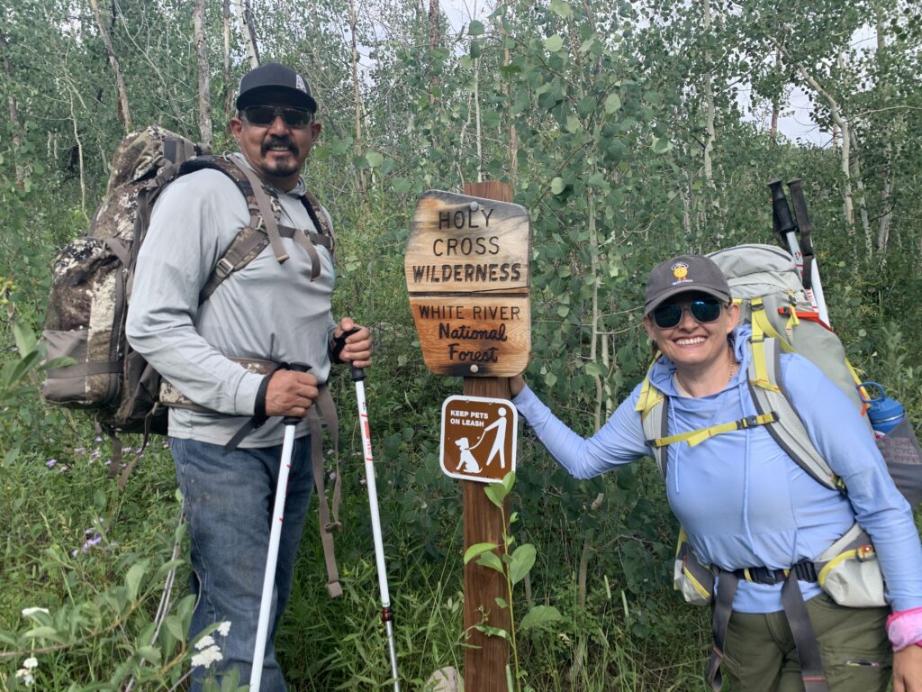 Two hikers with backpacks at the Holy Cross Wilderness trailhead sign in White River National Forest