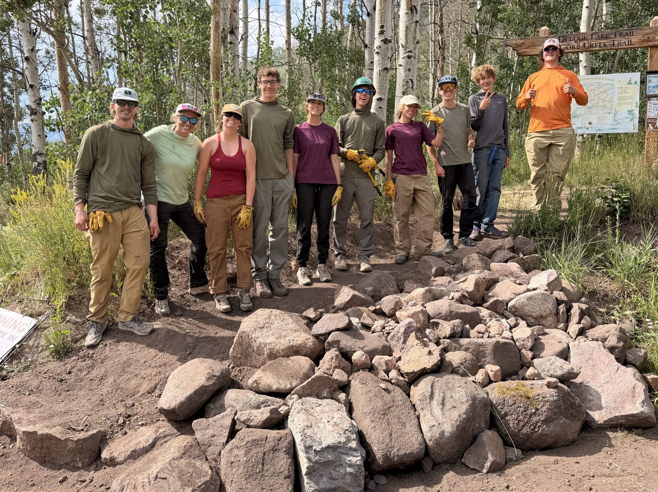 Eagle County Youth Corps crew standing over a finished rock step and rubble wall at a trailhead
