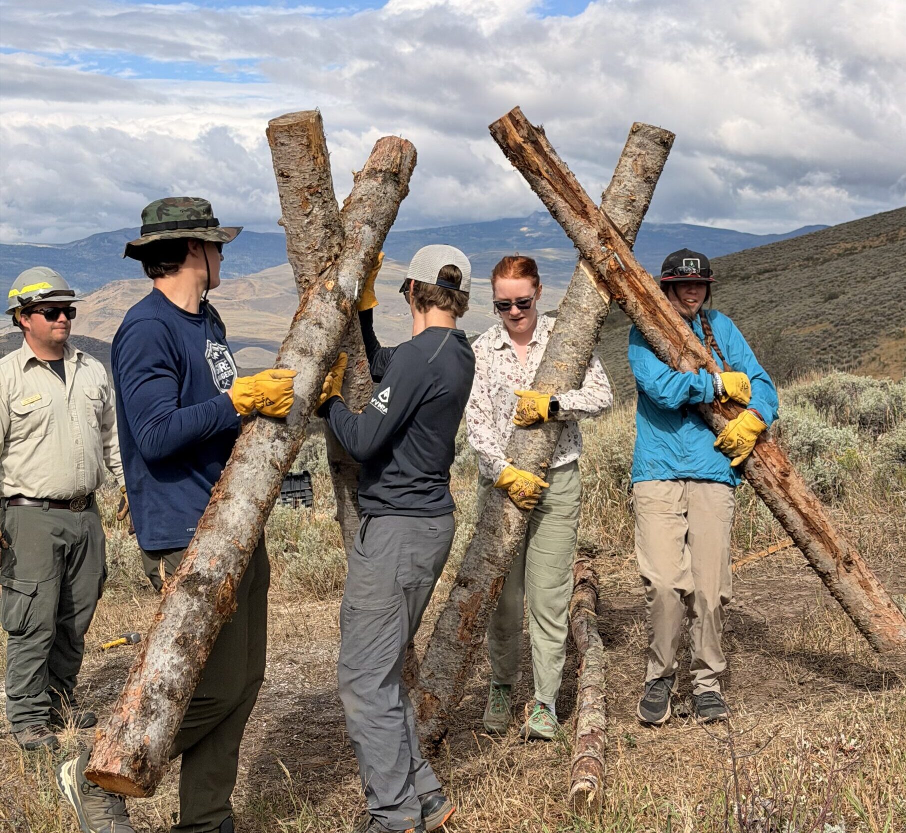 Eagle County Youth Corps crew members carrying crossed logs for a trail structure