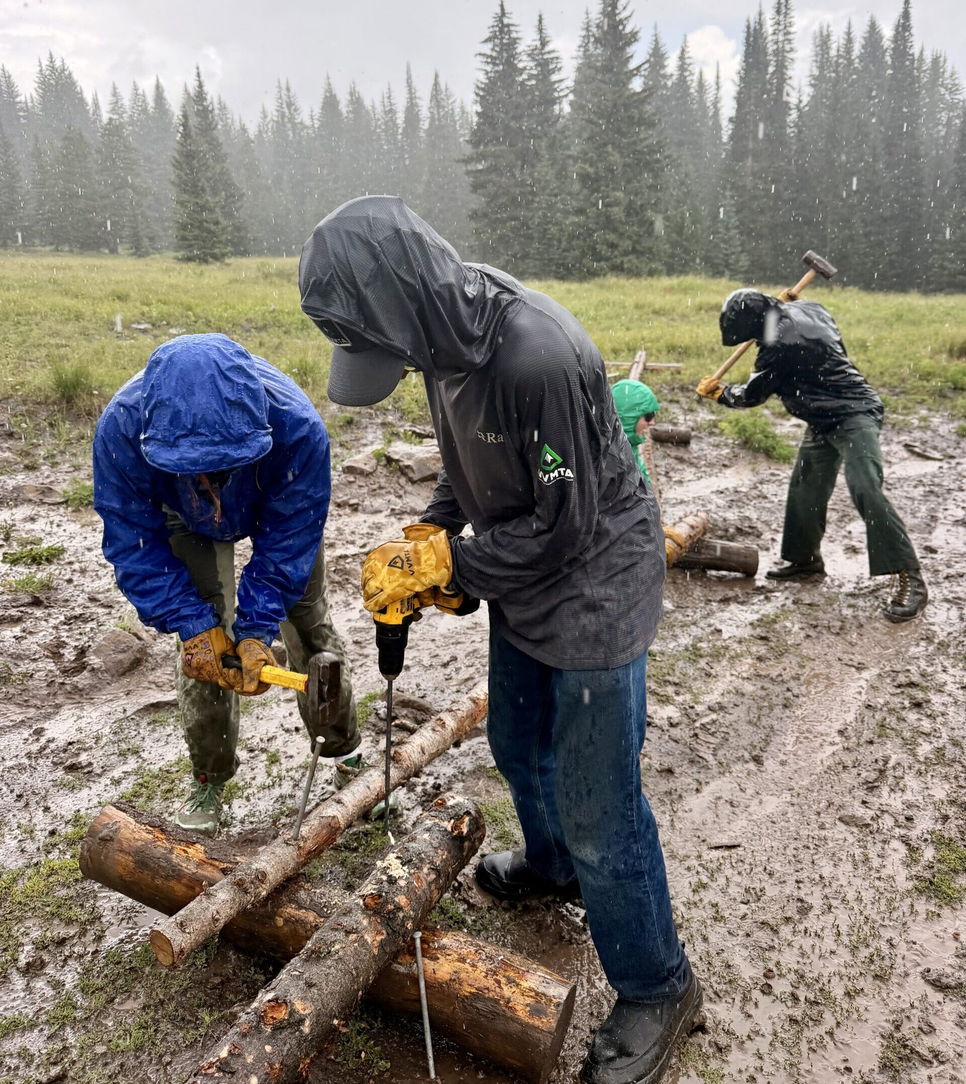 Eagle County Youth Corps crew members drilling trail structures during a rainstorm